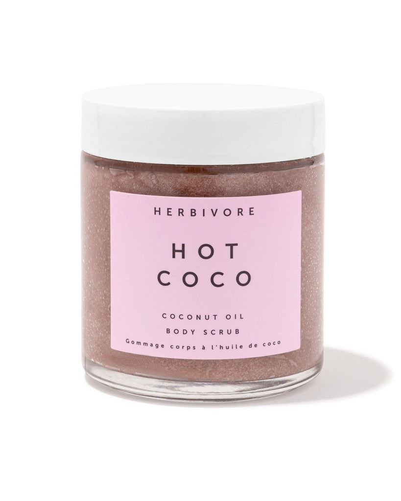 Herbivore Hot Coco coconut oil body scrub in a glass jar with a pink label on a white background